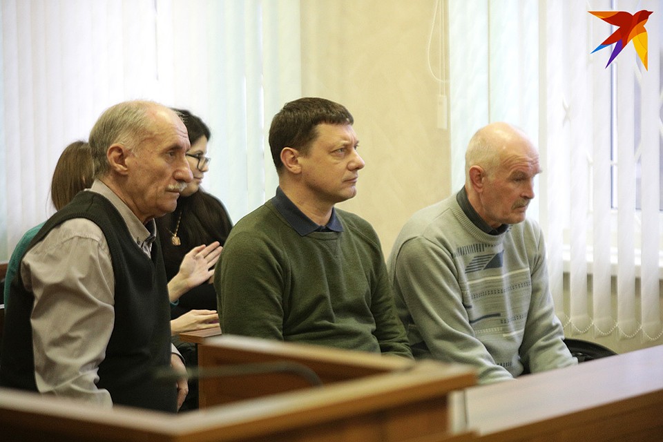 Клетка в зале суда пуста, трое обвиняемых сидят на первой скамейке.