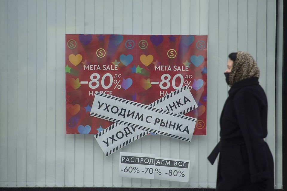 Женщина в медицинской маске проходит мимо объявления о распродаже